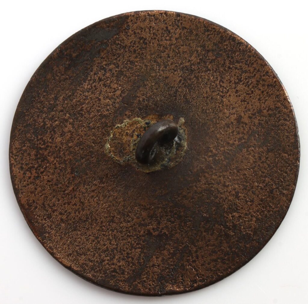 A round, textured copper disc with a central raised loop, displaying a weathered and aged appearance.