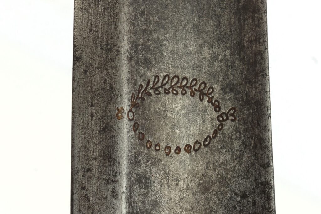 Close-up of a metallic surface featuring an intricate engraved design resembling a leaf and vine pattern.