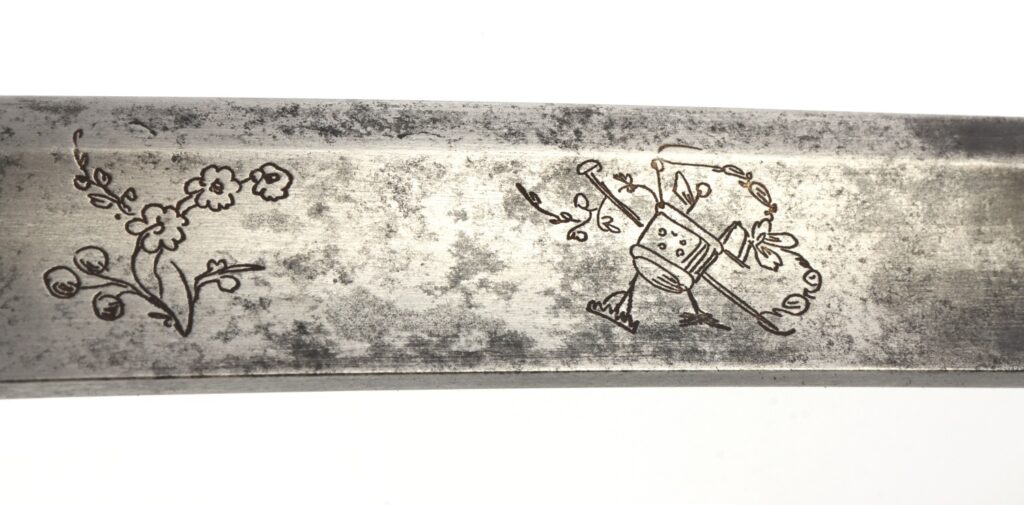 Close-up of a metal blade featuring decorative engravings of flowers on the left and a whimsical character with a watering can on the right.