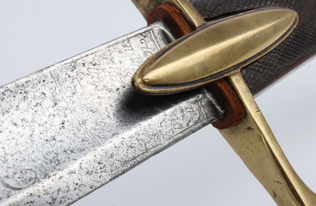 Close-up view of a vintage sword blade, showcasing intricate engravings and a brass guard.