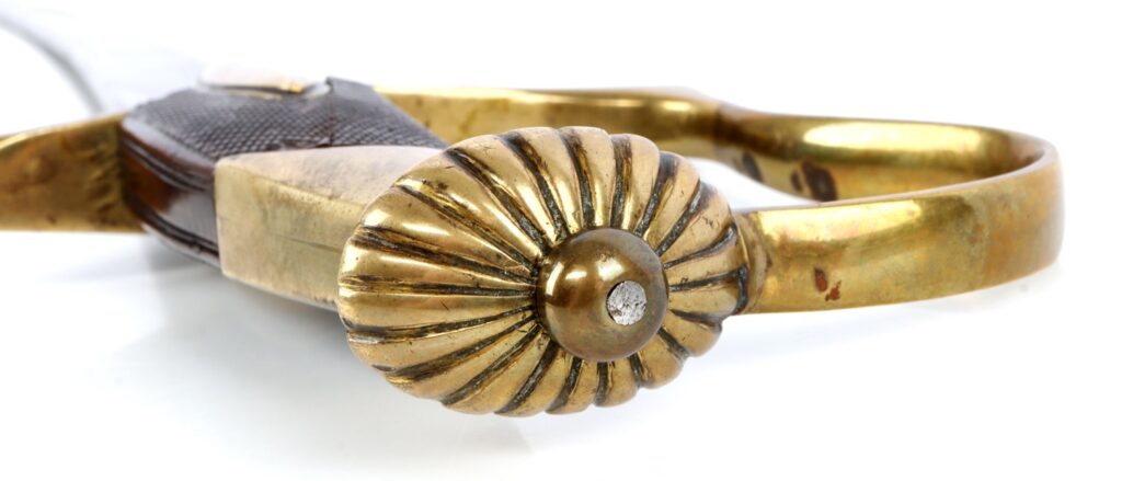 Close-up of an ornate brass handle with a decorative shell design and a leather grip.
