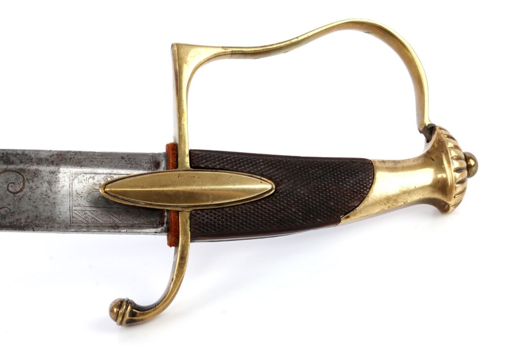Close-up of an ornate sword hilt featuring a brass guard and a textured grip, with an engraved blade partially visible.