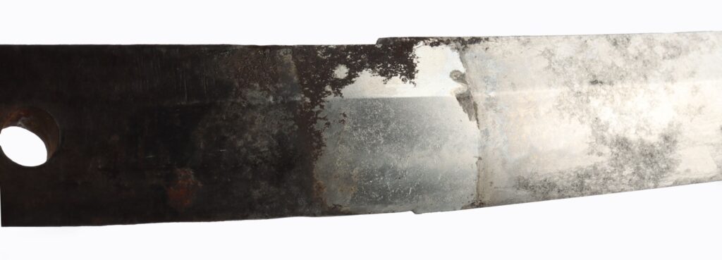 A close-up view of a rusty metal blade with a partially polished surface and a circular hole on one end.