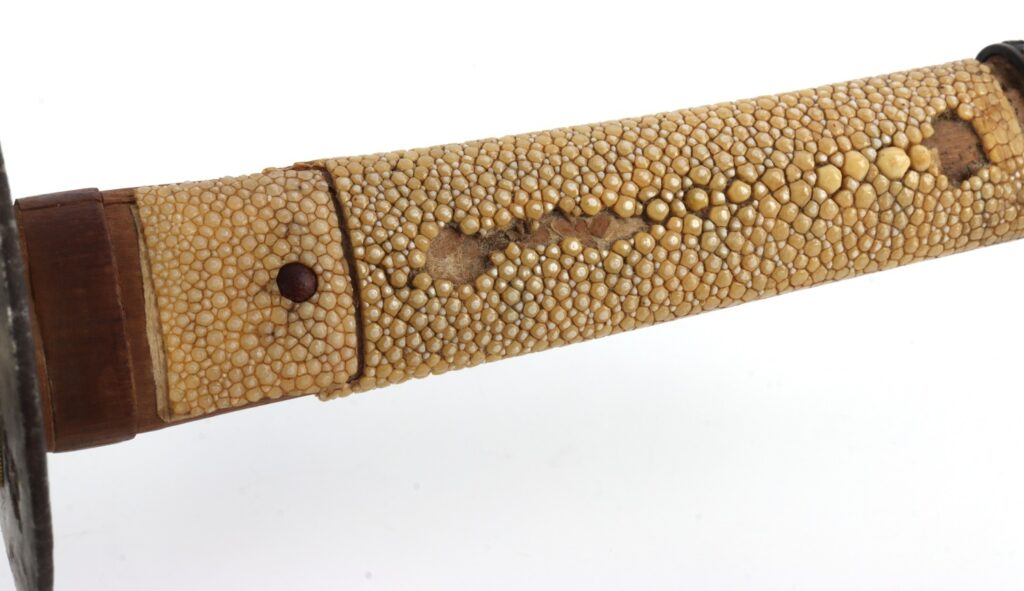 Close-up view of a sword handle wrapped in a textured material, showing small bumps and a wooden base.