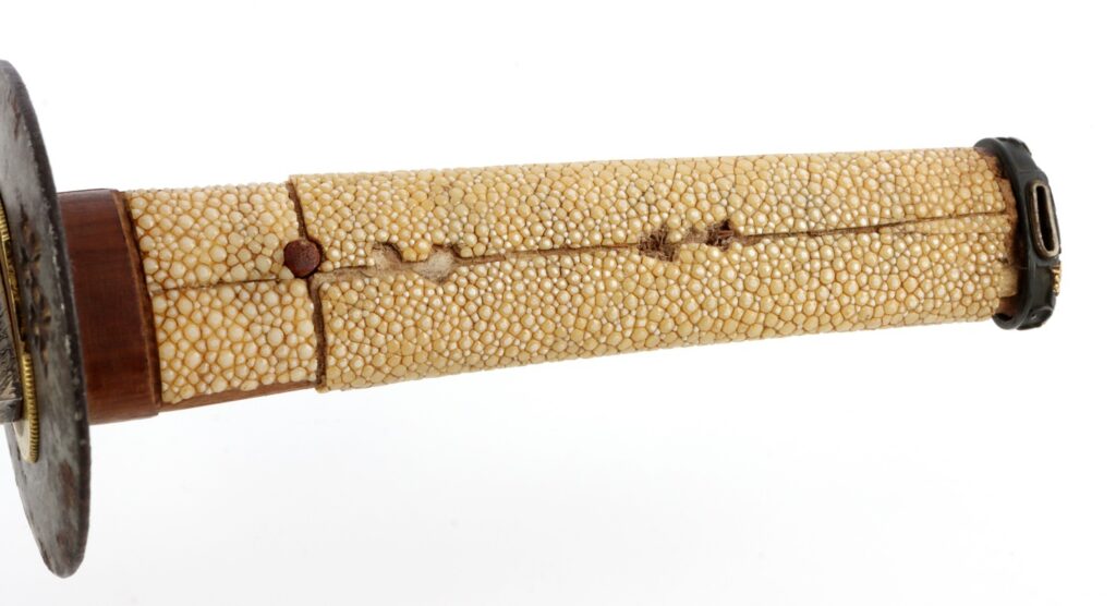 Close-up of a textured sword handle made from stingray skin, showing intricate details and a prominent tsuba.