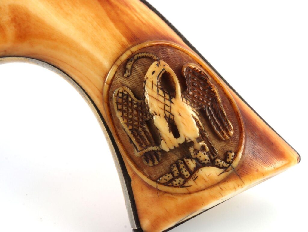Close-up of an ornate pistol grip featuring an intricately carved eagle design on ivory-like material.