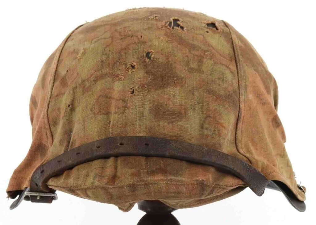 A worn and tattered helmet with a camouflage pattern and a leather strap, viewed from above.