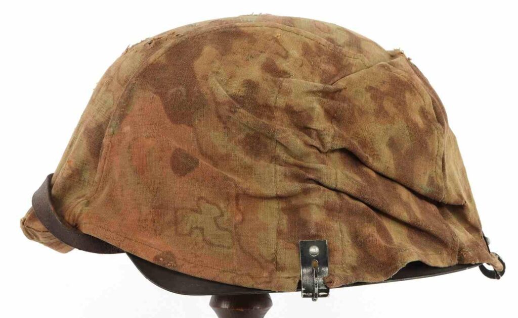 A vintage military helmet with a camouflage fabric cover, showcasing wear and tear, displayed on a stand.